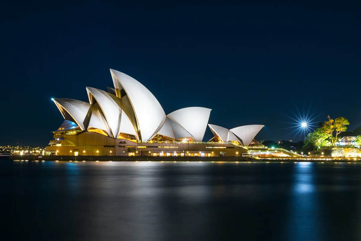 Ópera de Sídney iluminada de noche junto al agua